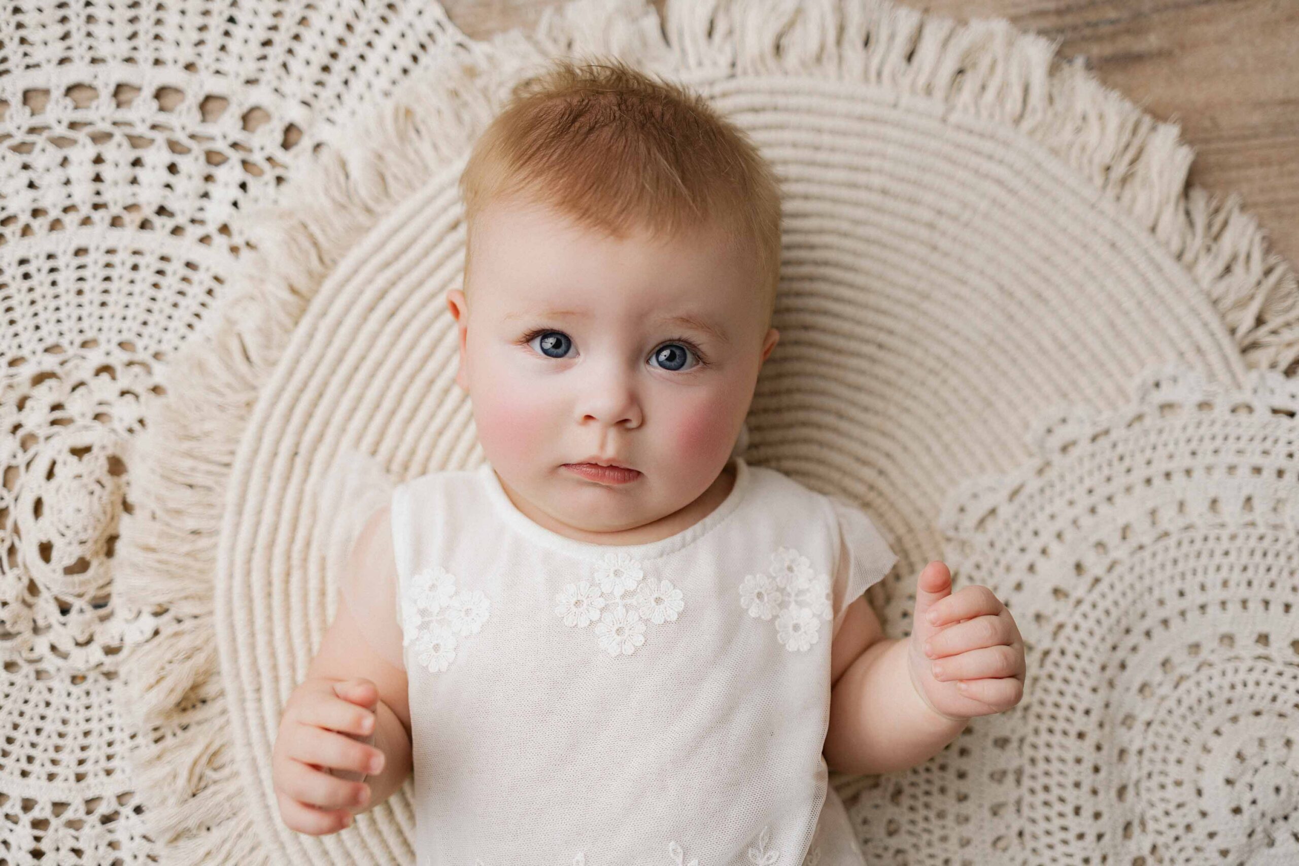 8 month old baby girl in Delray Beach lying on macrame doilies with bright blue eyes