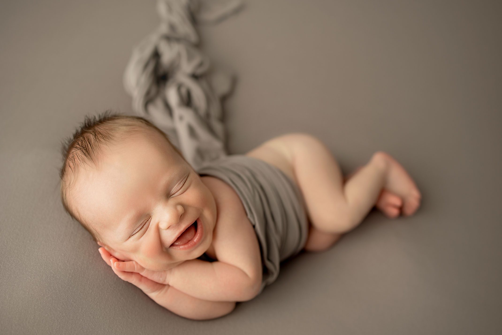 newborn baby boy lying on gray backdrop smiling