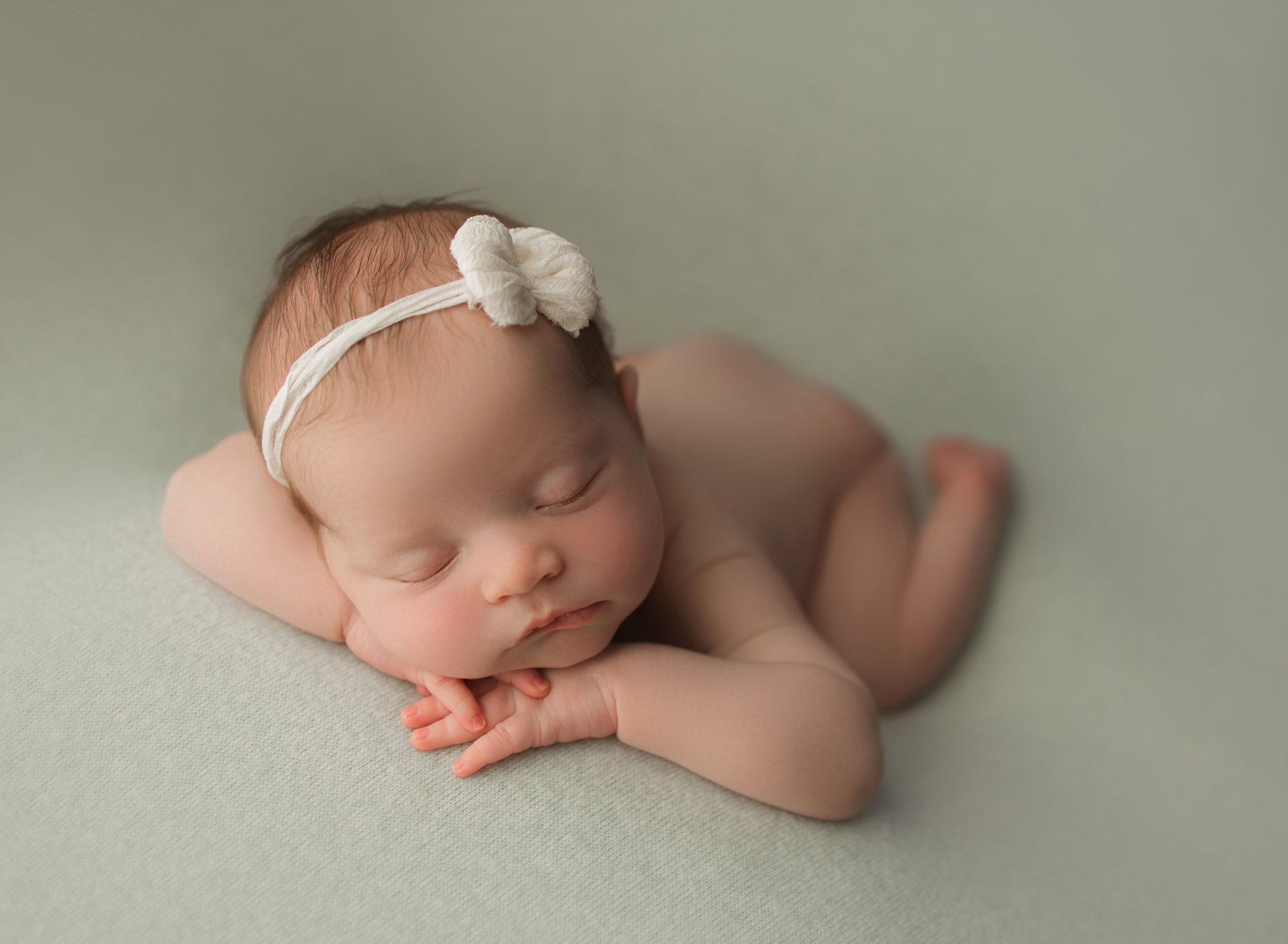 newborn baby girl on light green backdrop with white bow
