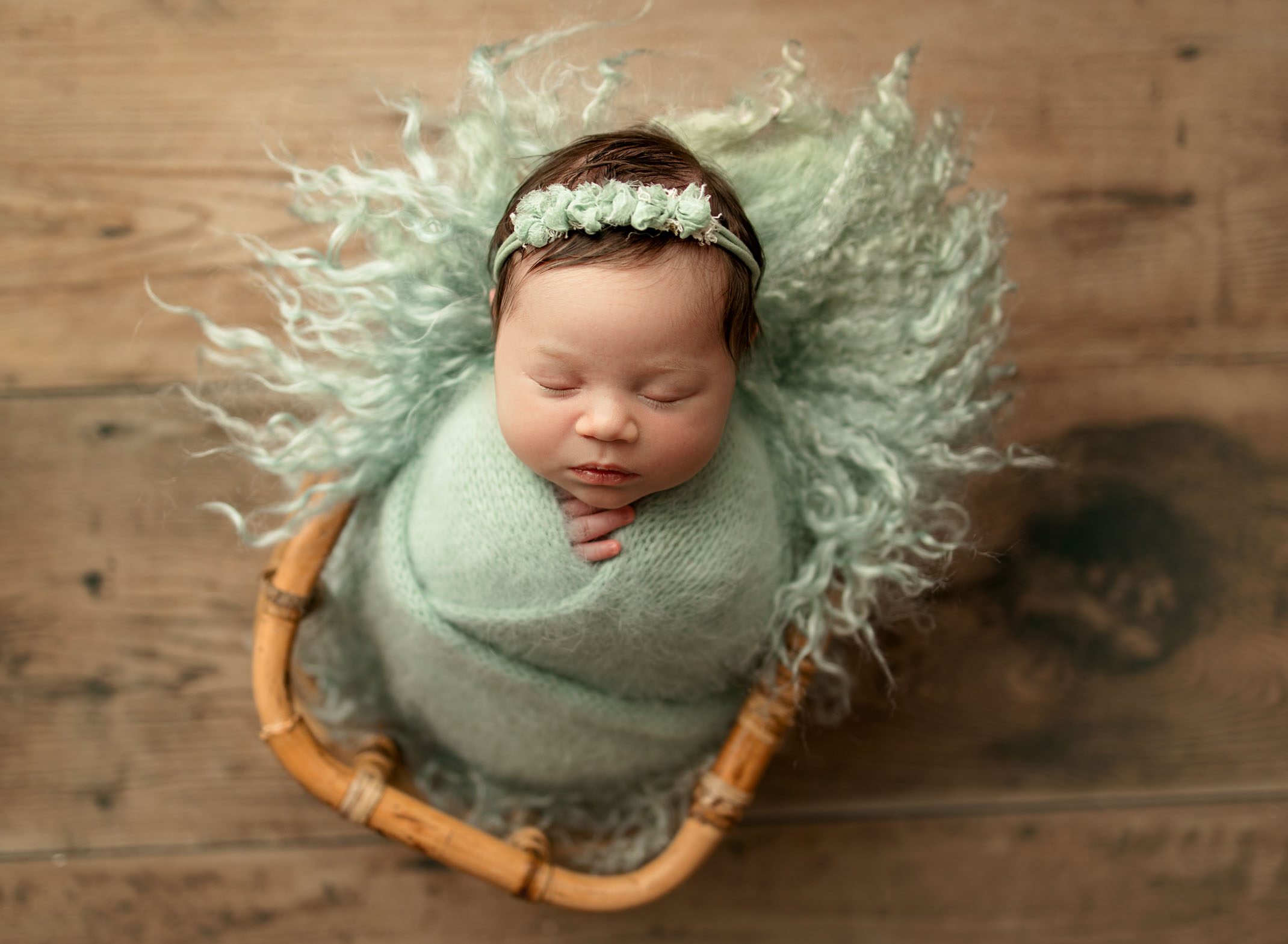 newborn baby girl lying in basket with sea foam green knitted wrap on seafoam green fur