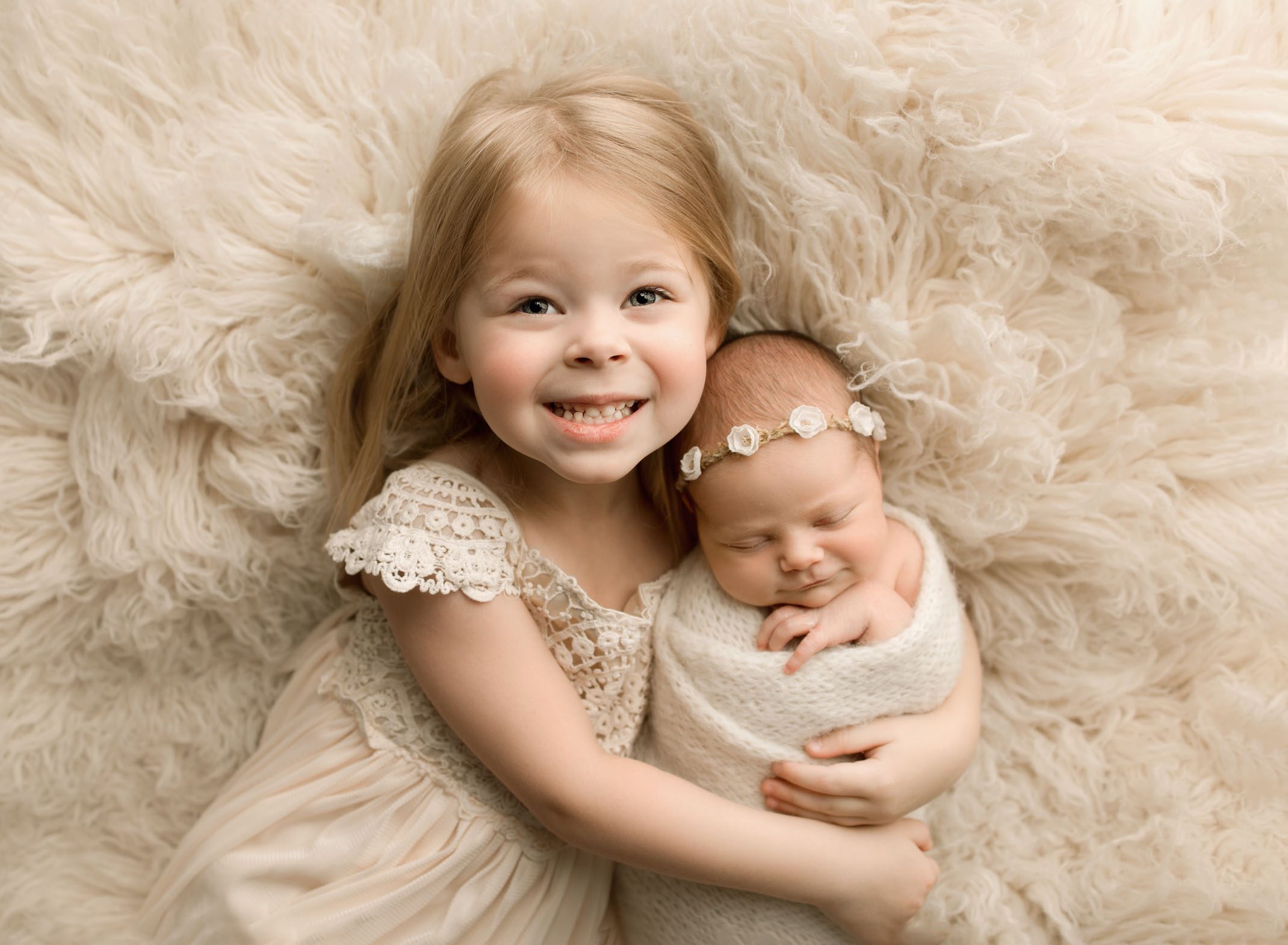 Newborn baby girl and her big sister lying on a fluffy white rug