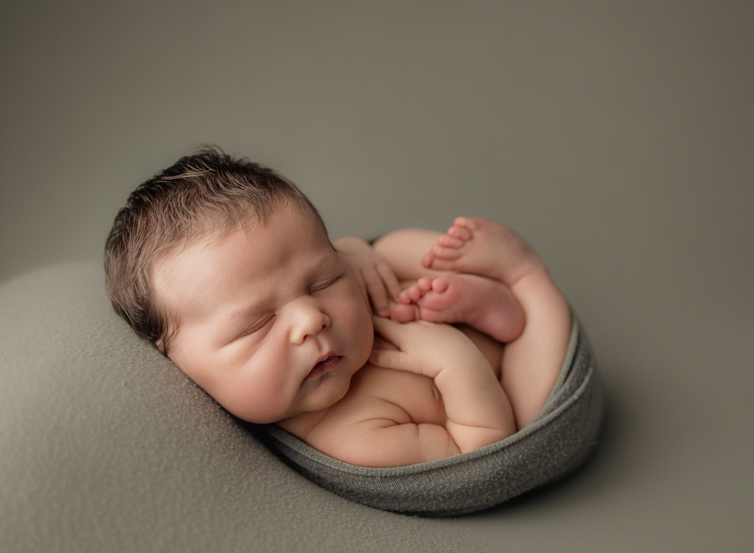 Newborn baby boy with lots of hair wrapped up in a green fabric lying on a matching green background