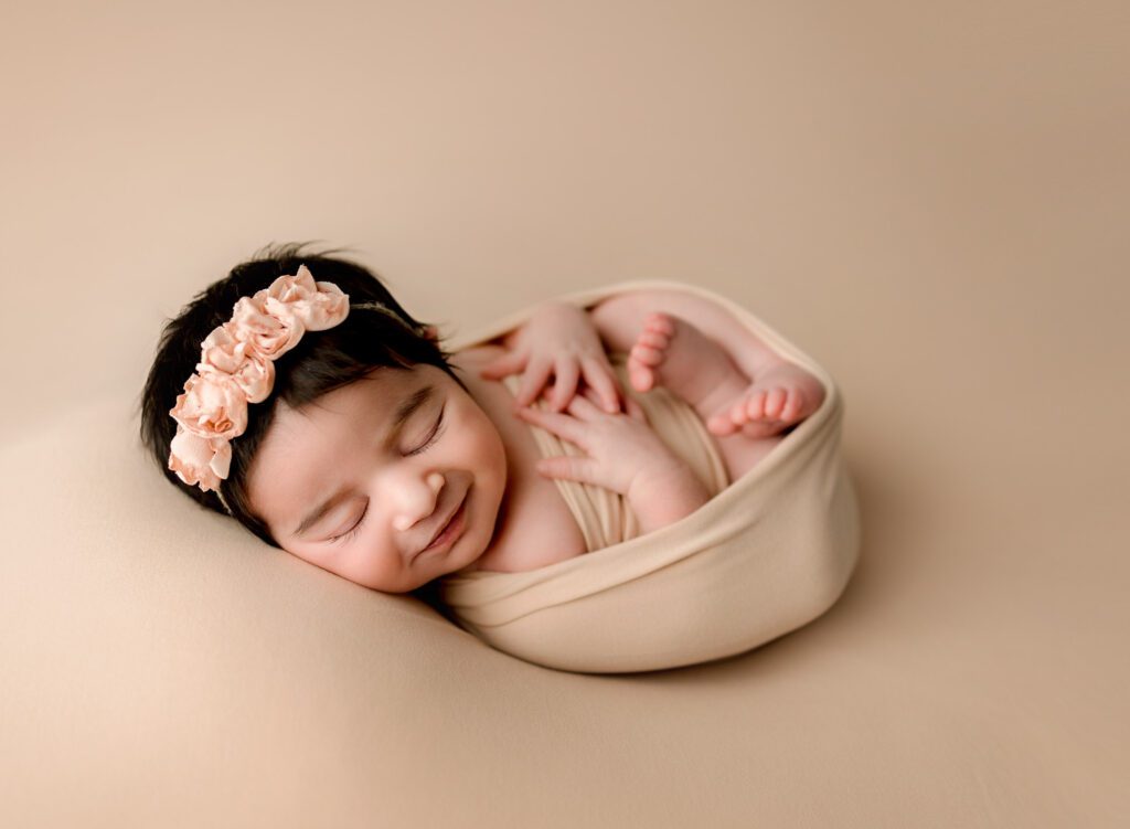 baby girl swaddled in neutral fabric smiling in her sleep during newborn photography Fort Lauderdale session