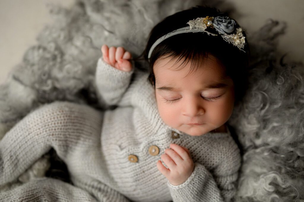 newborn baby girl wearing grey kntted onesie lying on fluffy rug during newborn photography Fort Lauderdale