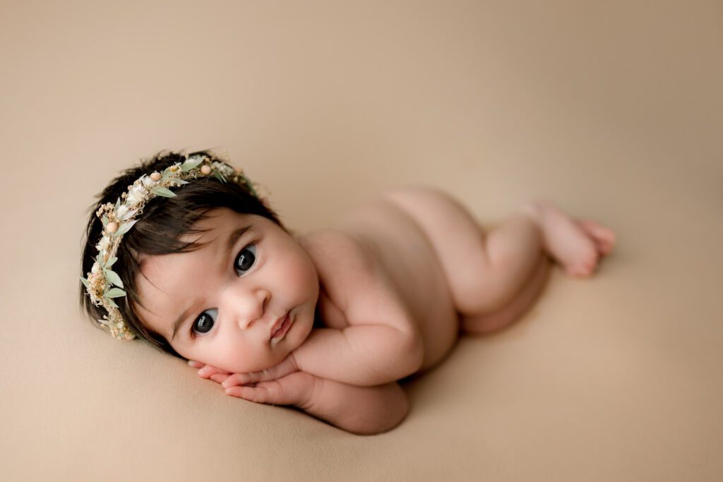 Newborn baby girl lying on a peachy/pink backdrop in the side-lying pose awake and adorable