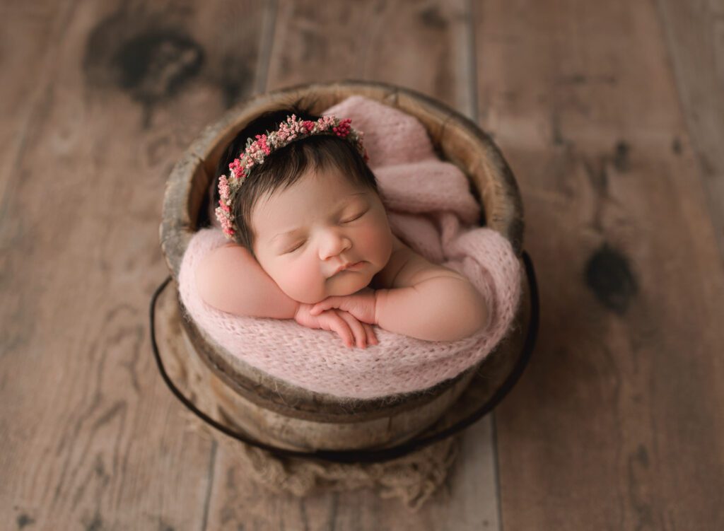 8 day old adorable baby girl posed in a wooden bucket with a pink blanket and pink floral crown