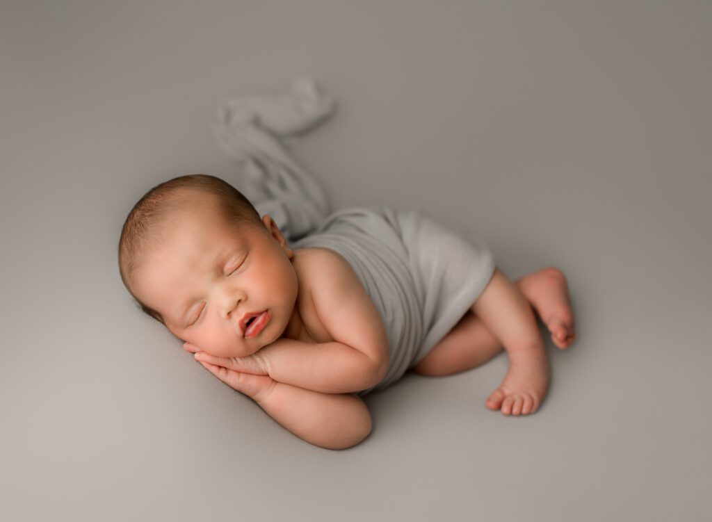 newborn baby boy lying on light gray blanket with hands under his cheek in coral springs newborn photoshoot