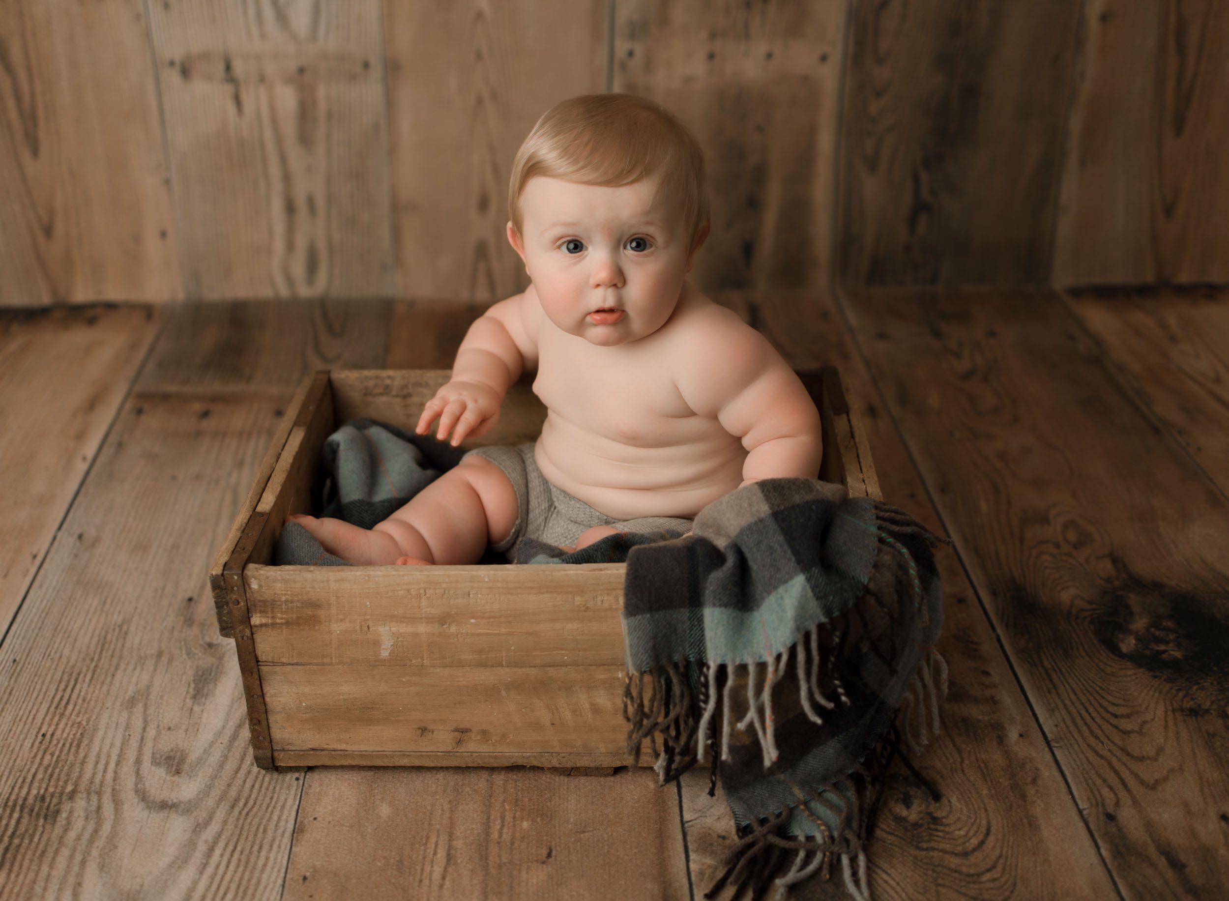 chunky baby boy sitting in box witih no shirt and a plaid blanket