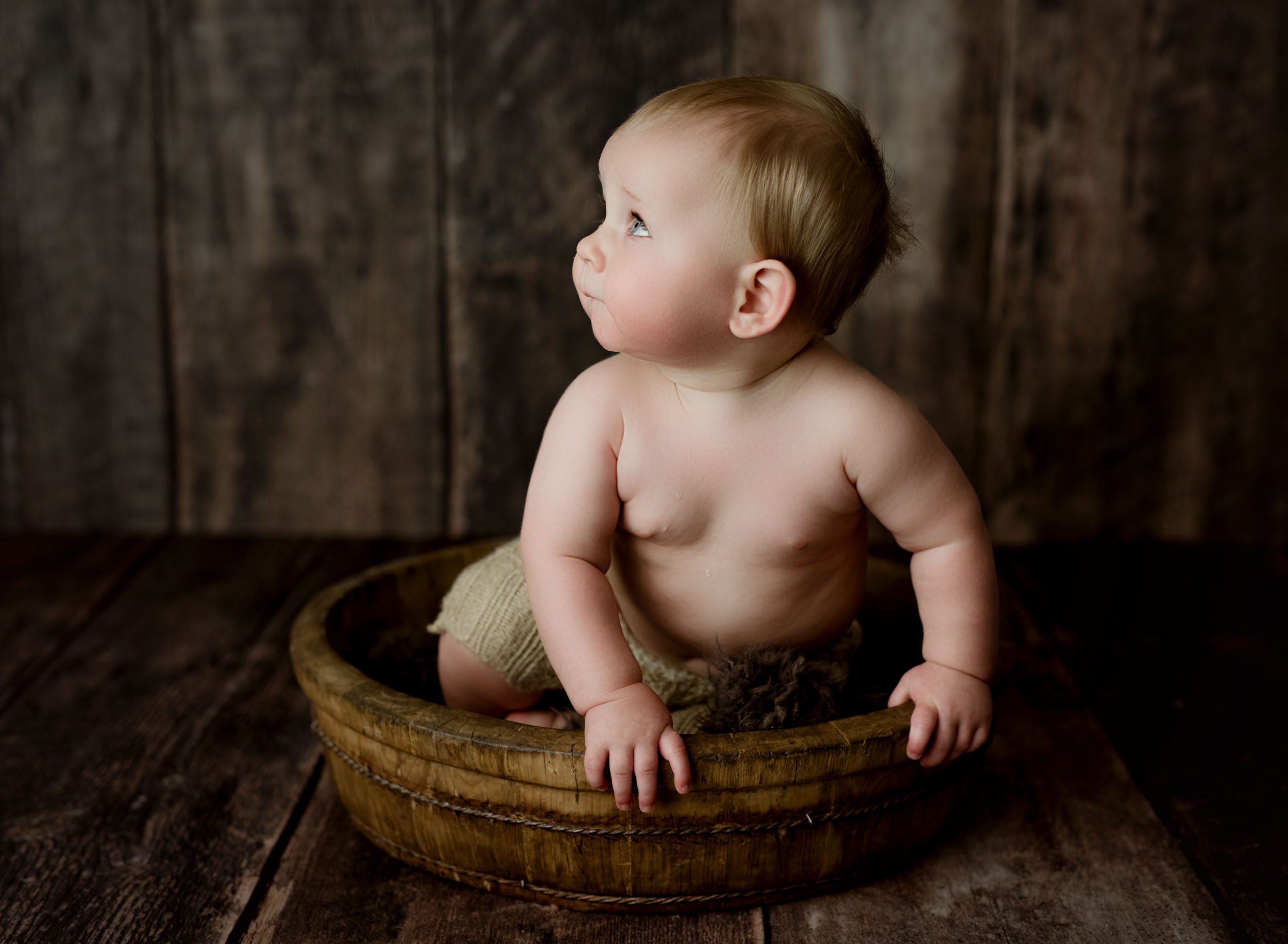 the cutest one year little boy sitting in a round bowl looking away