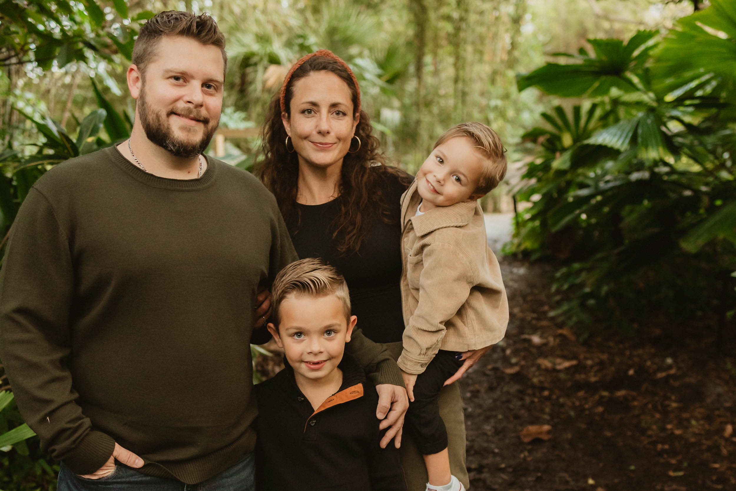 family of four standing closely together in lush park setting as a family photographer West Palm Beach takes their photo.