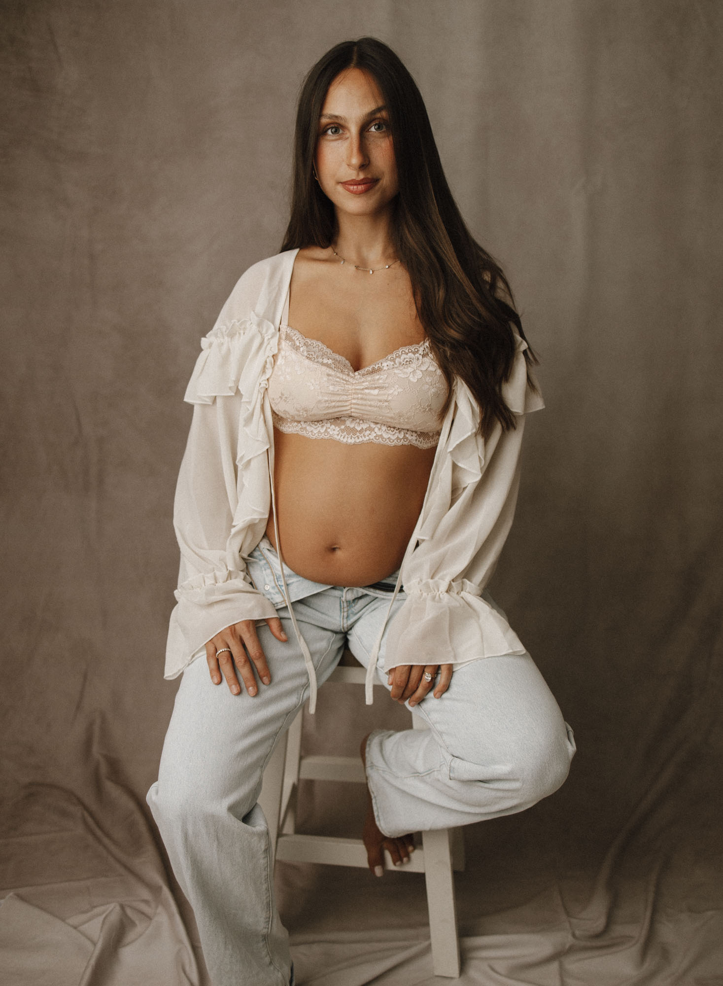 Parkland expecting mom studio photoshoot sitting on stool wearing flowy top and jeans