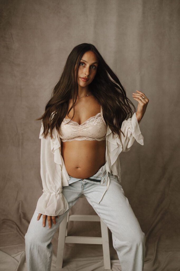 Mom sitting on stool looking sassy showing off her baby bump in soft fabrics and colors