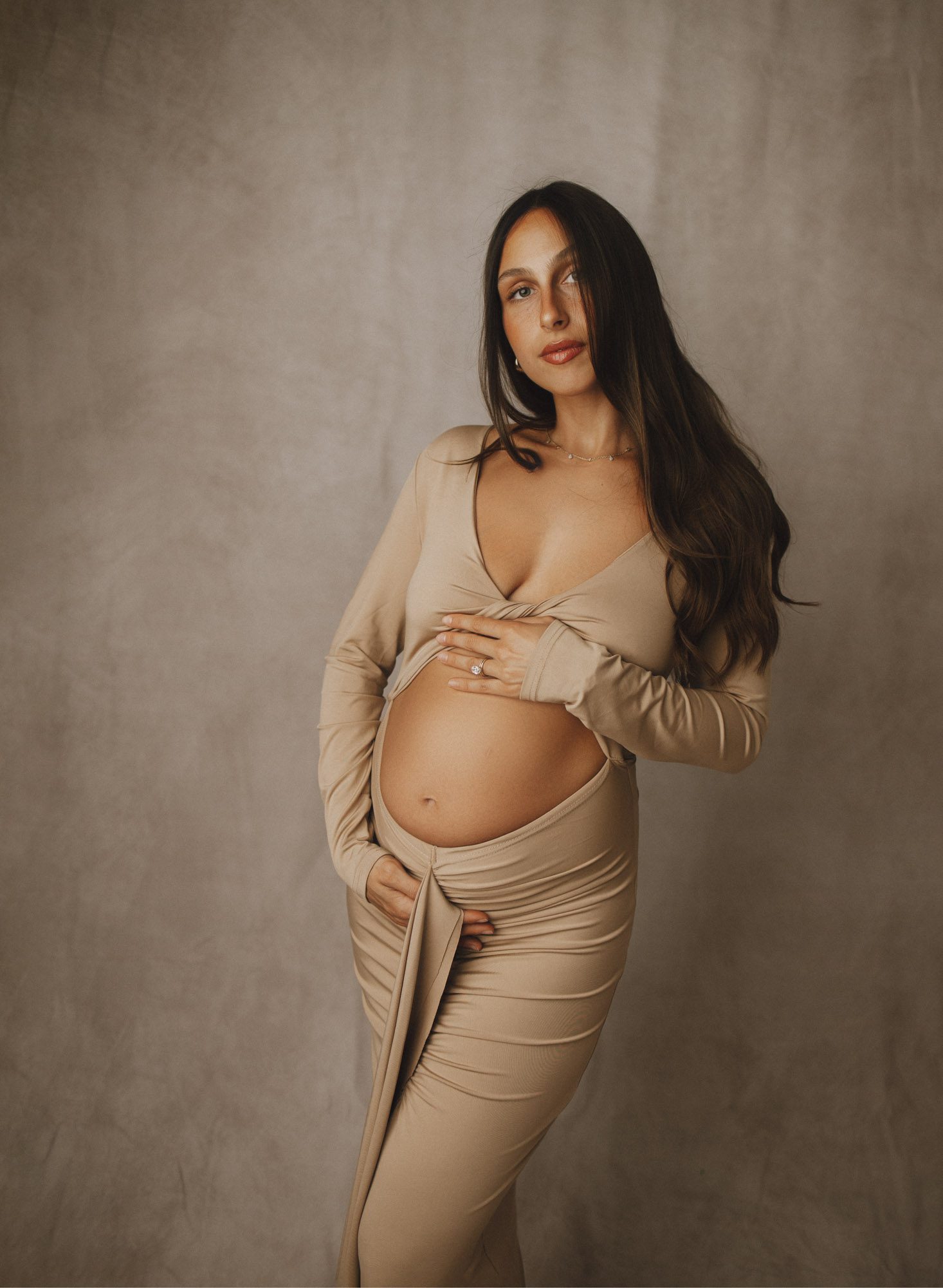 Photos of expecting mom on beige monochromatic backdrop/dress with her bump exposed.