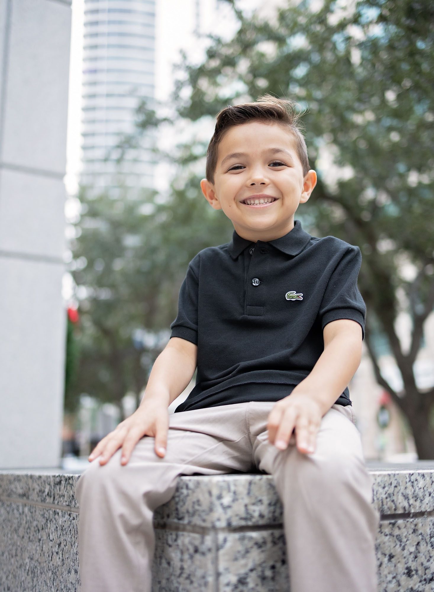 Little boy sitting on downtown Fort Lauderdale building pylon smiling big.