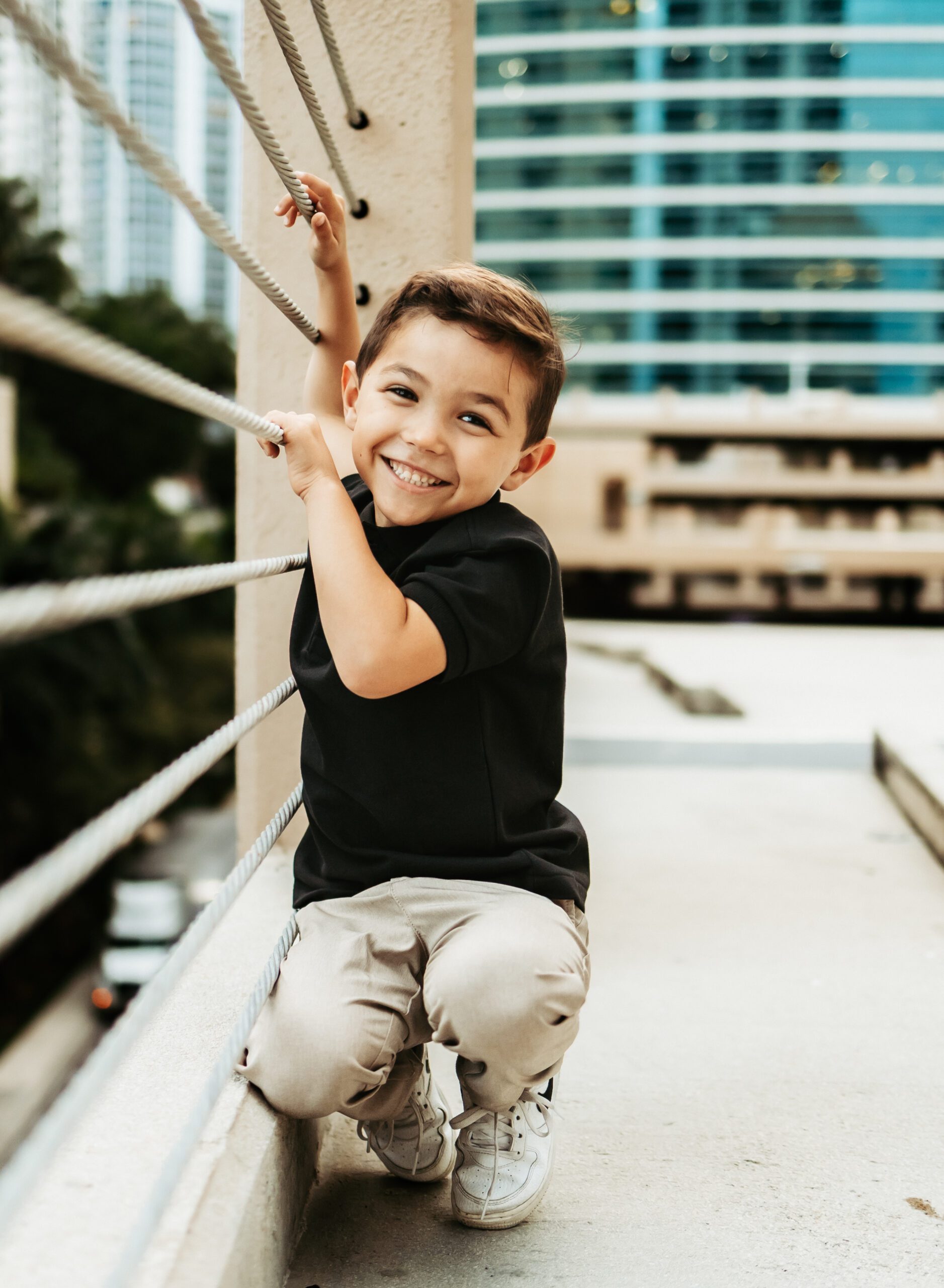 little boy holding onto to wire rope smiling at camera