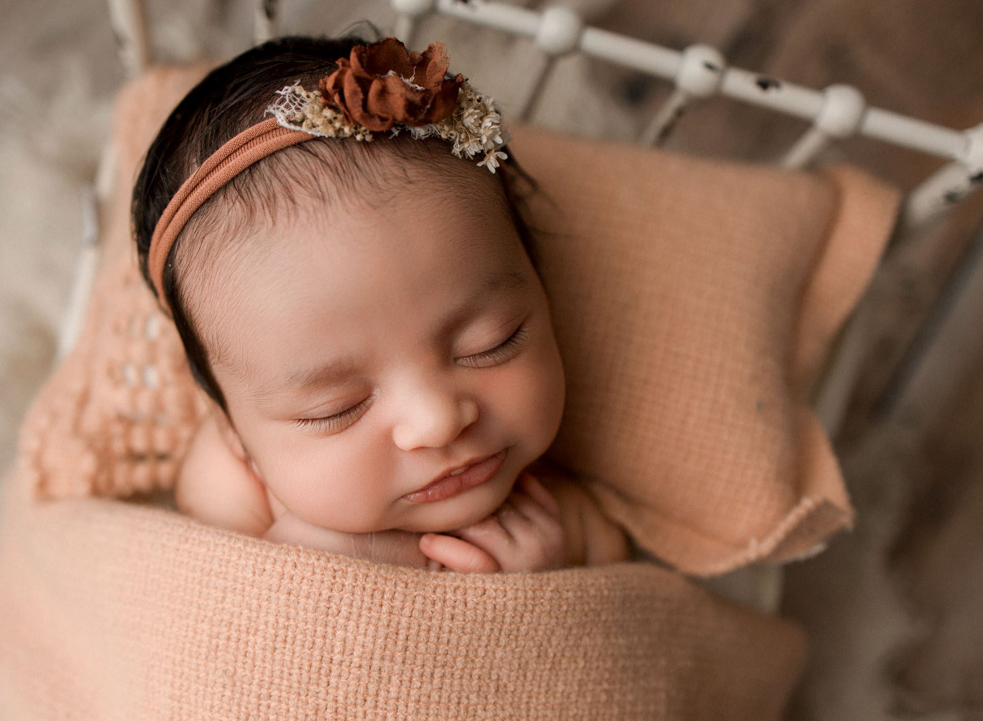 Parkland newborn baby girl lying on a white bed with peach bedding.