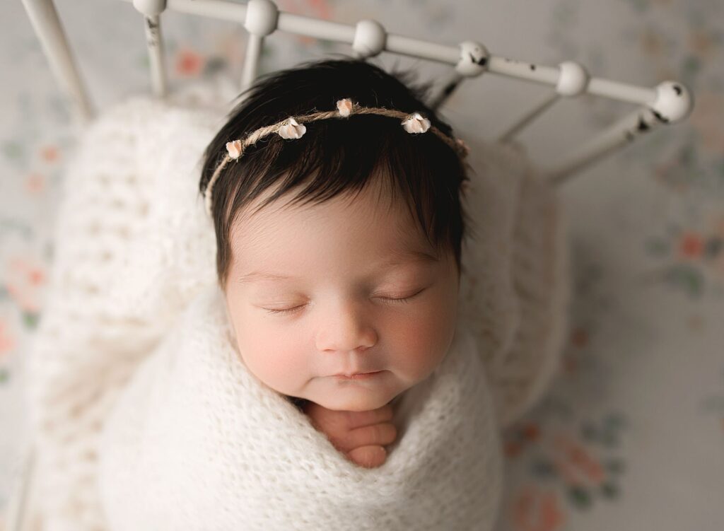 newborn baby girl in metal bed tucked in with cream knit wrap durin her newborn photos Parkland.