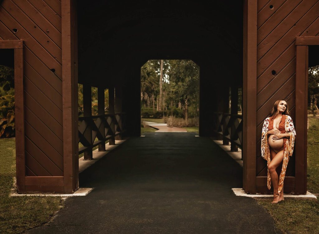 Pregnant mother leaning against a barn wearing a robe with belly exposed