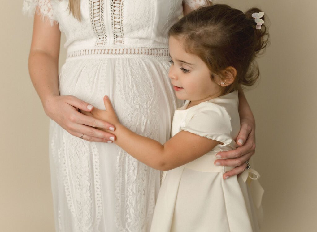 mother and daughter cuddle baby bump with a soft cream background