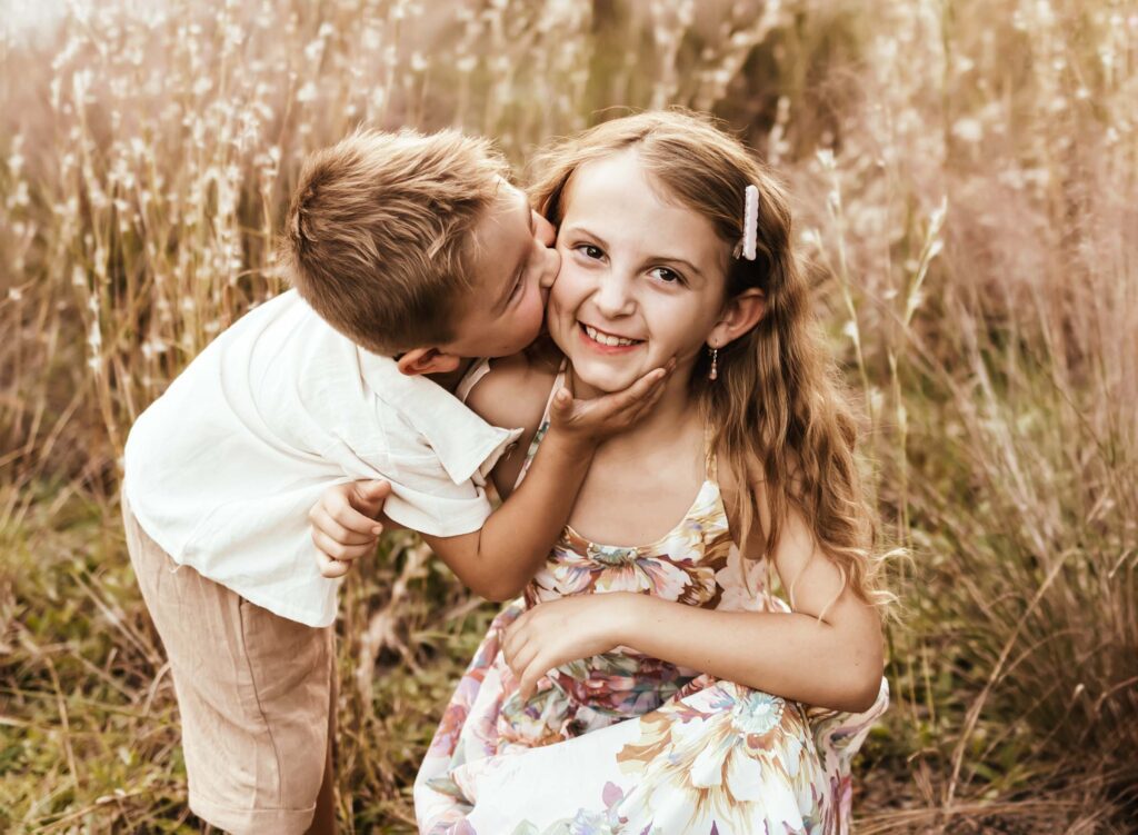 Little brother kissing big sister on the cheek at their family photoshoot in tall grass