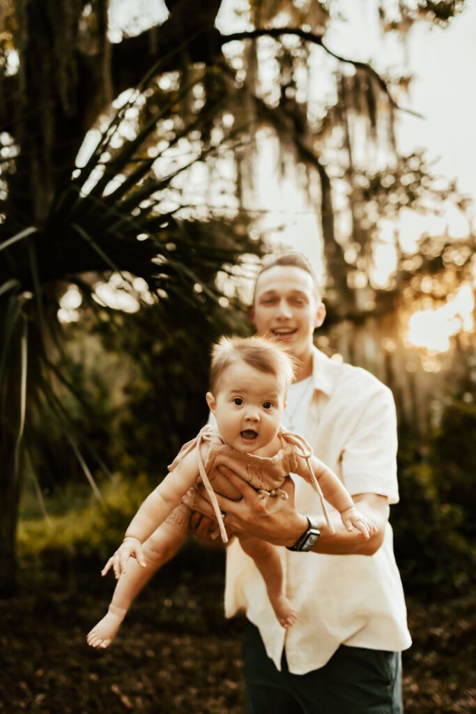 A good family photo idea is Dad holding baby like an airplane for family photos at golden hour.