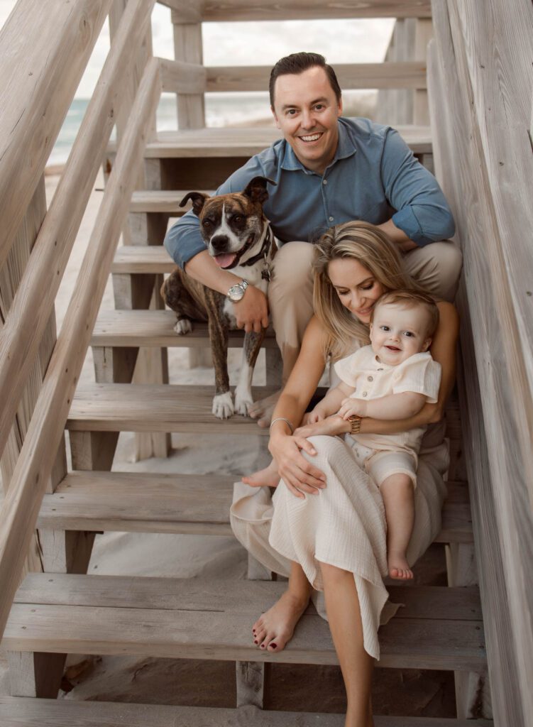 Family with their dog sitting on stairs at the beach for their family photoshoot in Palm Beach