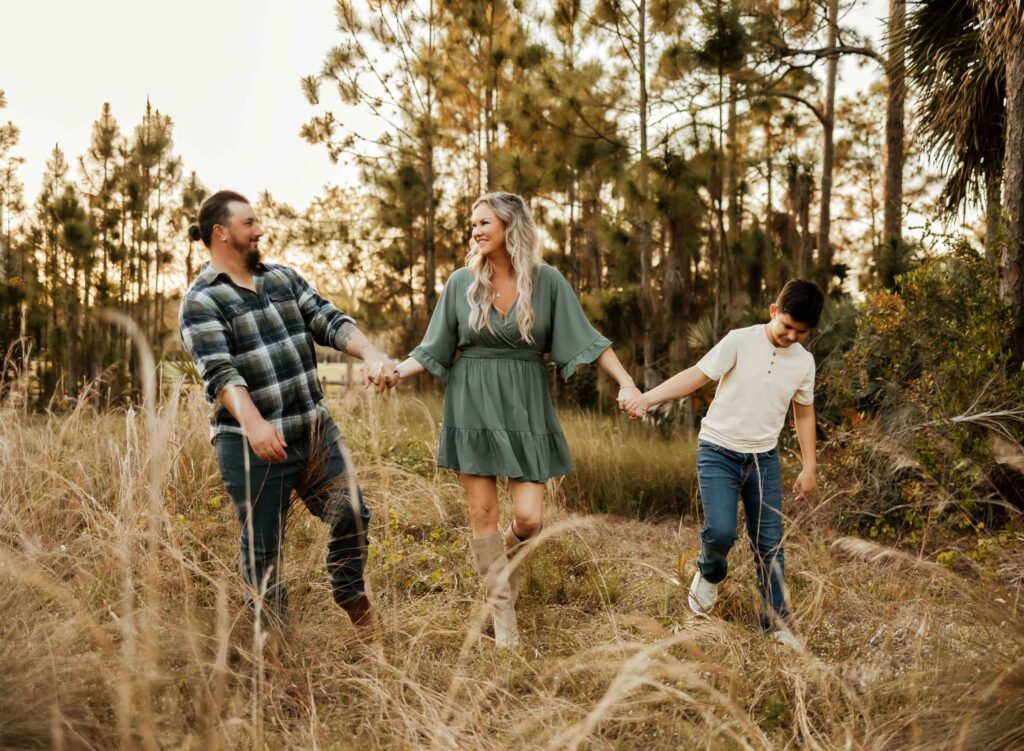 Family holding hands and walking through grass at golden hour at their outdoor family photos in West Palm Beach