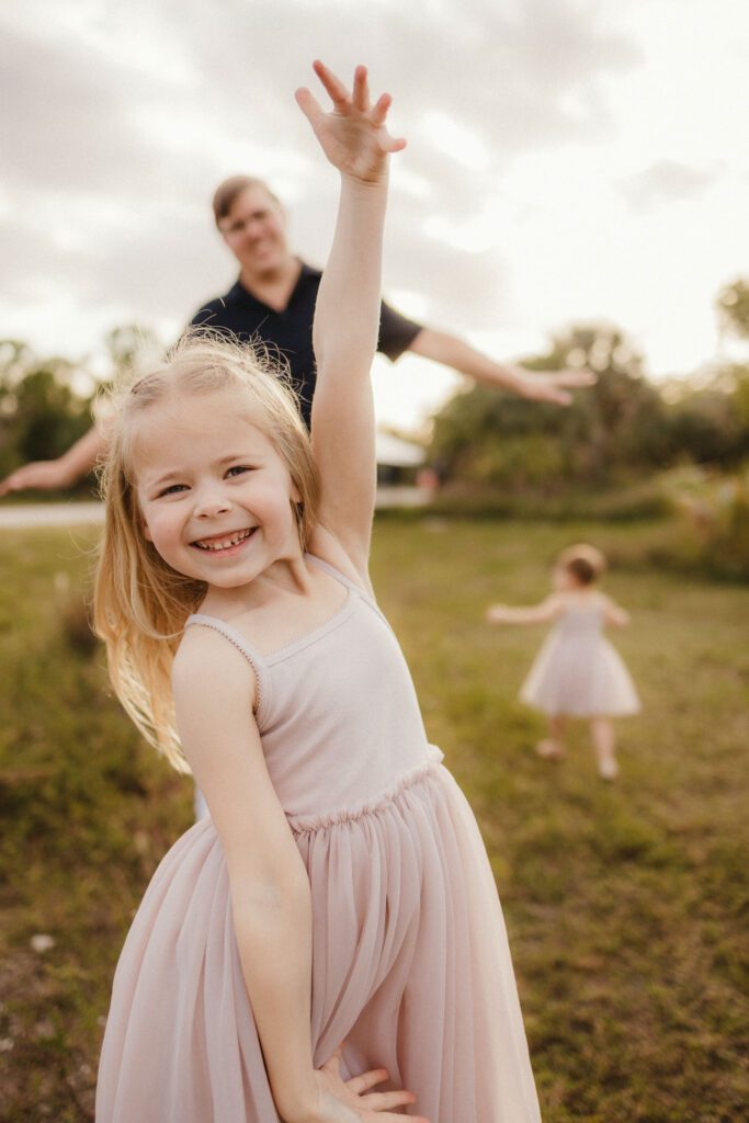 Big sister cheesing for the camera with dad and sister being silly behind her for family photos