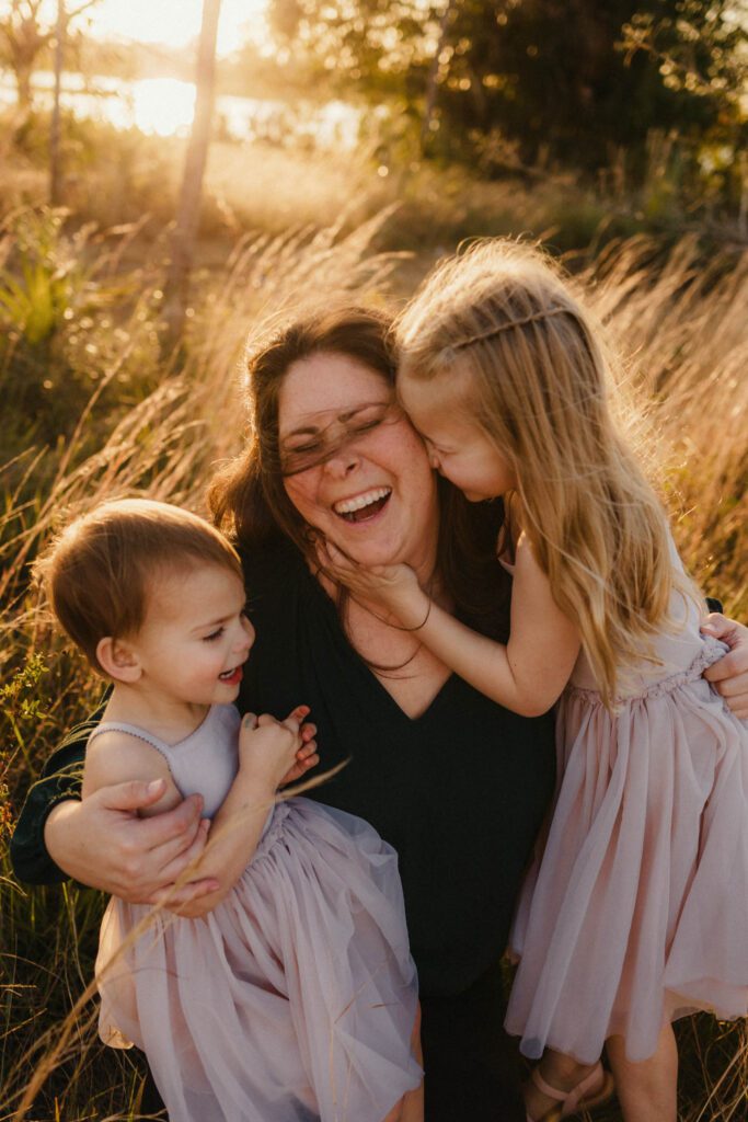 Mother and her daughters in silly snuggle laughing at an outdoor family sunset photoshoot