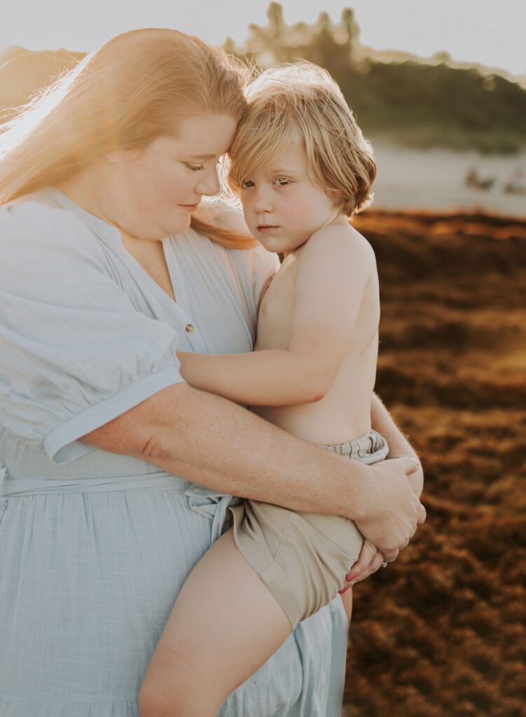 Mom holding toddler son snuggling for touching moment at golden hour