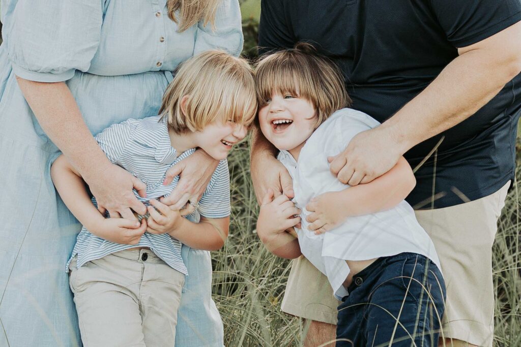 An outdoor family photo Idea where parents tickle brother for silly laughter for photos
