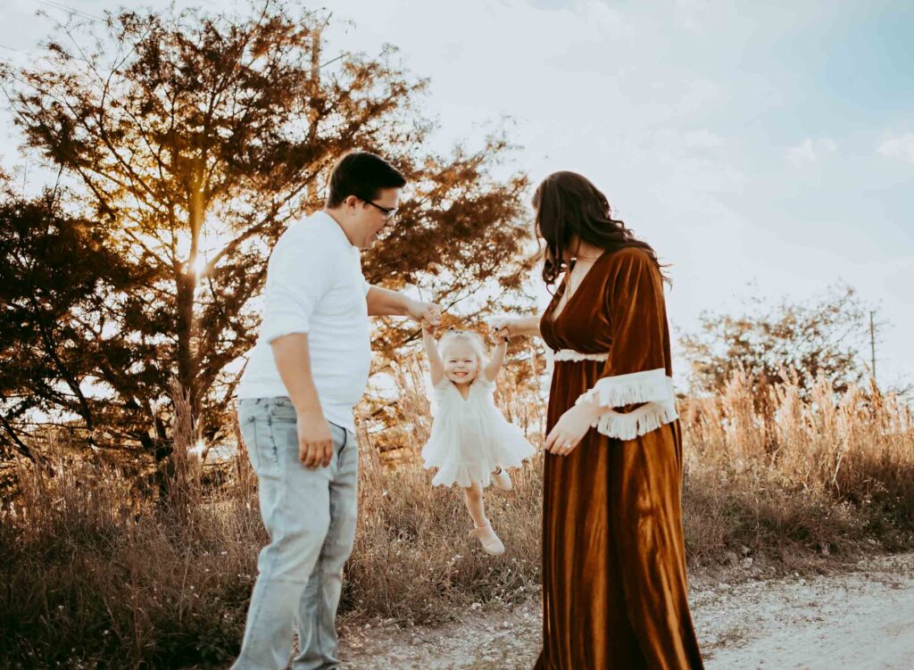 Mom and dad swinging their little girl in the air together at a dramatic golden hour