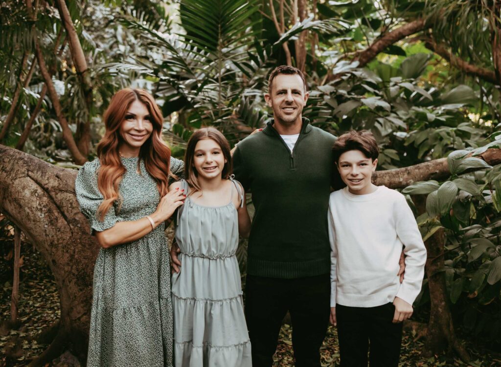 Traditional family photo of parents and tween son and daughter with lush tropical backgrond