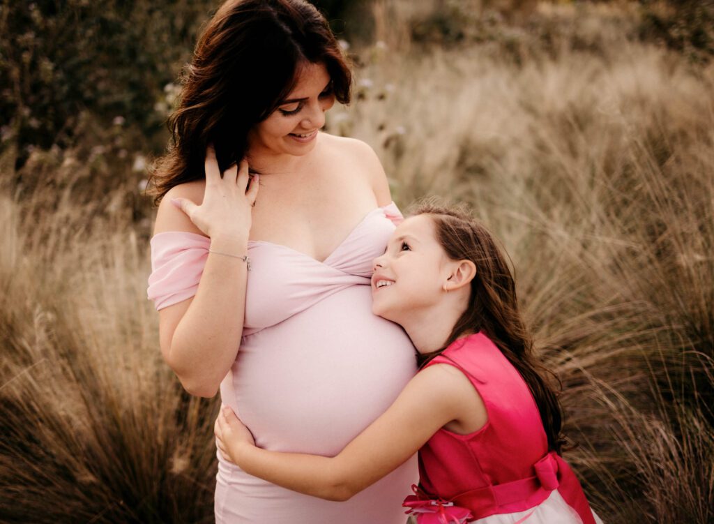 big sister hugging mom's baby bump in tall grass
