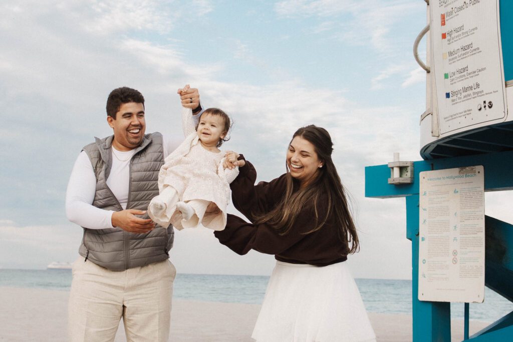 Mom and dad swinging baby at the beach and baby has big smile
