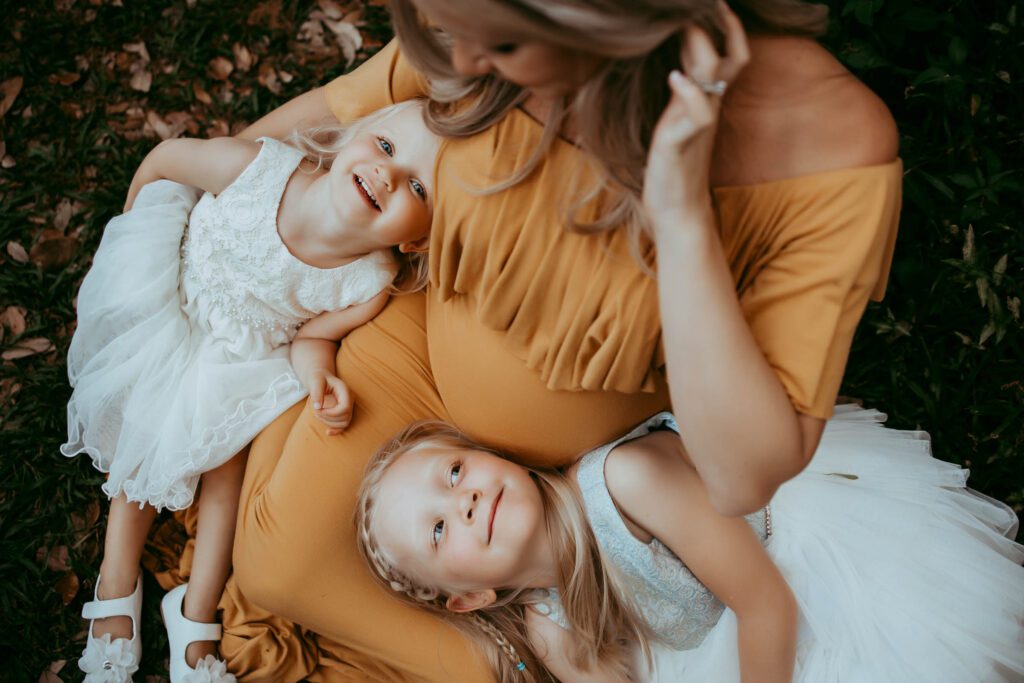 maternity photoshoot ideas for siblings lying in pregnant mothers lap looking up and smiling