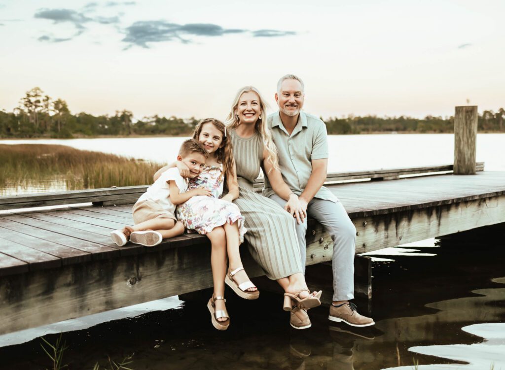 Quick family photo idea for family of four sitting on a dock at blue hour right before sunset.