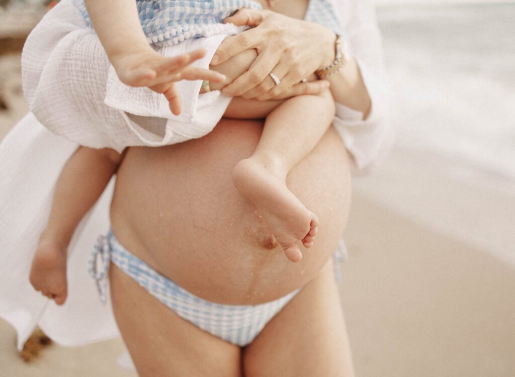 close up shot of pregnant mom on the beach holding toddler for pregnancy announcement photos