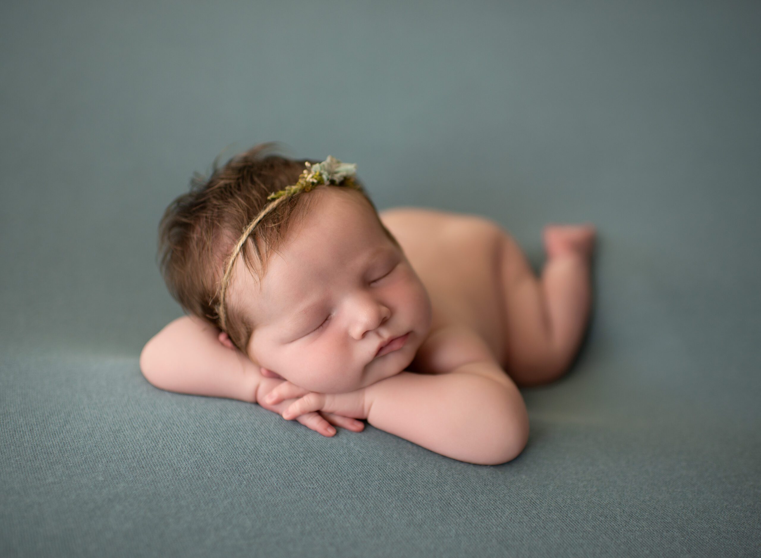 newborn baby girl lying on green backdrop with her head on her hands in Parkland Florida